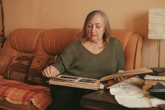 Senior lady looking at old photographs in the album, remembering her past and her baby, family.