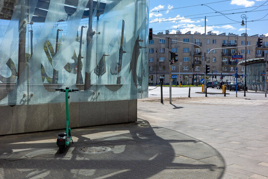 Warsaw, Masovian Voivodeship, Poland - April 23, 2026: A modern city street featuring a green electric scooter parked by a glass architectural structure.