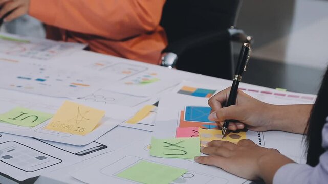 Asian women working together as web designers in an office, pointing at whiteboard with uxui mobile app wireframe