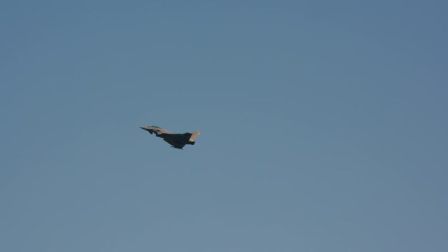 Military fighter jet in straight level cruise against pale blue sky showing full profile with wing and canard detail, slow motion