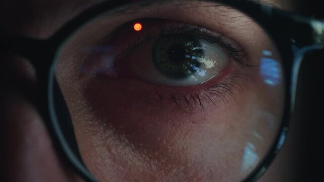 Information overload reflected in human eye behind glasses as glowing screen light flickers in pupil. Close up Eye scans endless data and news feeds showing information overload and digital stress.
