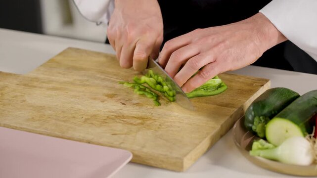 chef cutting green pepper on a wooden board