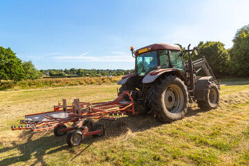 Fototapeta premium Agricultural Tractor Raking Hay on Field in East Sussex, England, UK near Bodiam Village