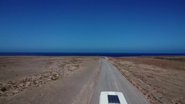 Sandy shore of Fuerteventura with gravel road and camper van driving towards the camera
