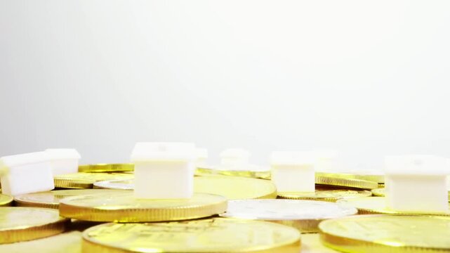 Cinematic 3D animation featuring a house placed on stacks of rotating gold and silver coins symbolizing wealth, investment, and financial stability. The smooth rotation and metallic shine create a pow