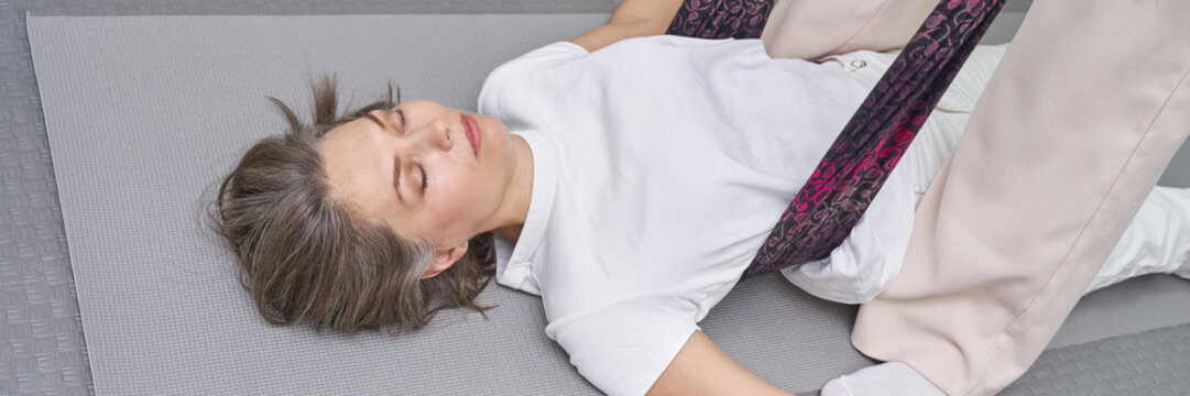 Woman lying on mat using strap for hip support during stretching exercise illustrating physiotherapy and wellness routine