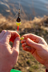Hands preparing fishing bait on hook with float in background © Olha Semeniv