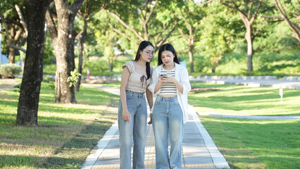 Naklejka premium Young Women Walking and Using Smartphone in Green Park
