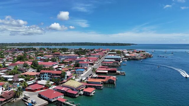 aerial drone view of Isla Col&oacute;n in Bocas del Toro Panama, showcasing crystal-clear turquoise waters, lush tropical vegetation, and colorful Caribbean-style buildings along the coastline. 