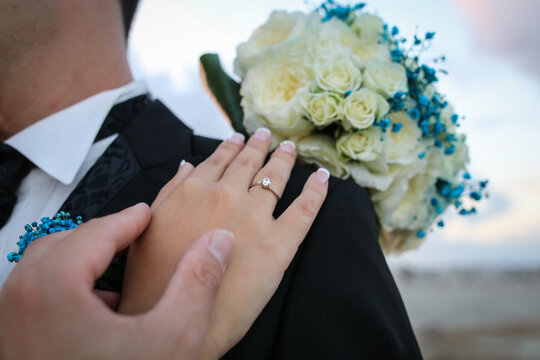 Una pareja acaba de casarse. La mujer lleva la alianza de boda en su mano y el ramo de flores. Posa su mano sobre el novio.
