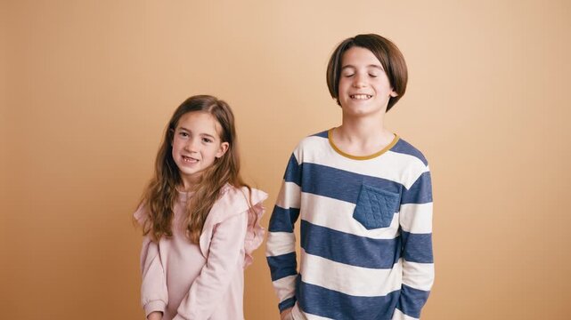 Adorable siblings smiling and laughing while posing in a studio. The cute little girl and her older brother are gesturing with their hands