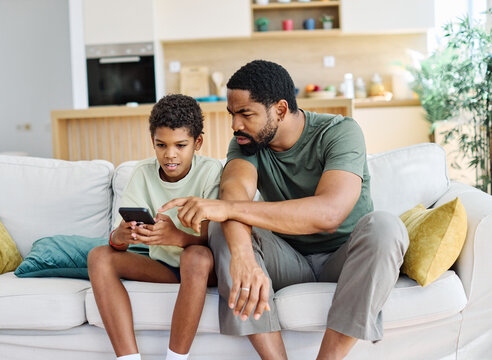 Teenage boy sitting at sofa with his father and using phone. Father and son bonding and having fun at home