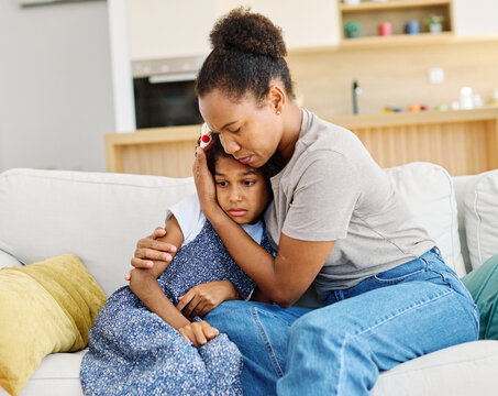 Mother embraces daughter on a couch at home while comforting her after a difficult day. Sharing secrets and problems, support and parenthood concept