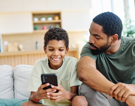 Teenage boy sitting at sofa with his father and using phone. Father and son bonding and having fun at home