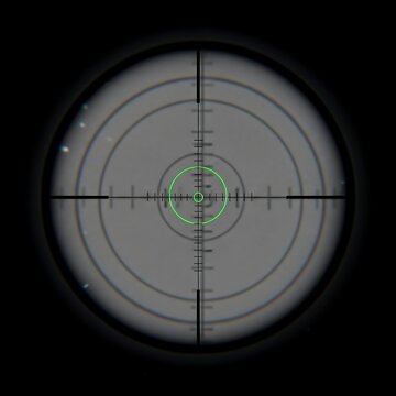 Crosshairs on a target through a telescopic scope, showing range markings and illuminated reticle