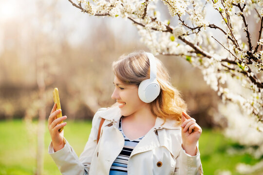 Woman with headphones looking at mobile phone. Modern connection and digital communication in flowering garden.