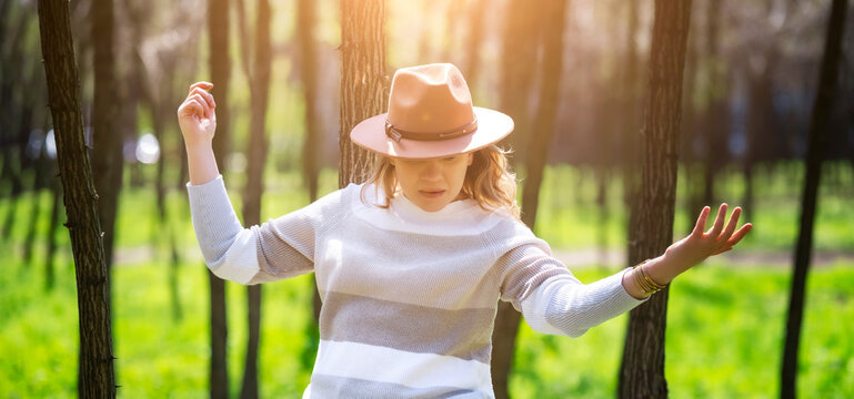 Active woman in hat dancing in forest. Carefree spirit and connection with nature.