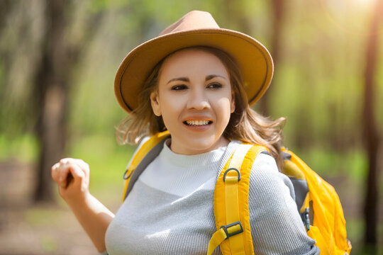 Woman in hat with backpack hiking in forest. Adventurous lifestyle concept for travel and outdoor recreation