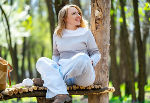 Relaxed woman sitting on wooden platform in forest. Digital detox concept and peaceful mood.