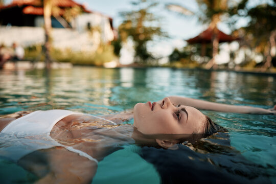 A woman floats on her back in a bright pool, relaxed and serene, capturing a lifestyle moment by water that conveys calm, wellness, and vacation vibes in an outdoor setting.