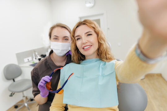 Happy female dentist with satisfied customer patient taking selfie at dental clinic