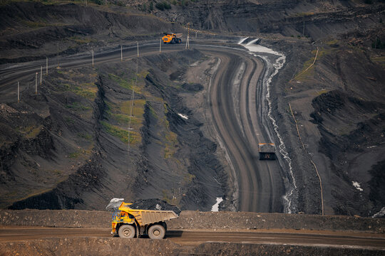 Expansive open pit mine with heavy machinery operating on rugged terrain, truck with coal