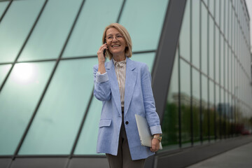Fototapeta premium Successful mature business woman talking on phone, holding laptop
