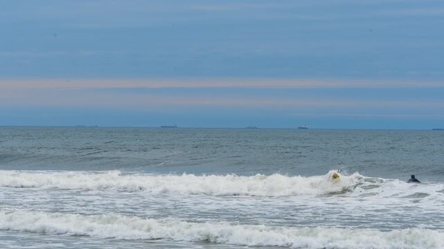 Several surfers are in the waves near the shore. Surfing on a dull cloudy day.