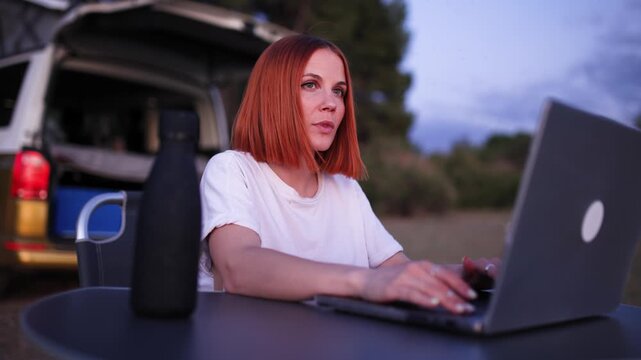 Young freelance woman working remotely on her computer during a van life road trip. A digital nomad enjoying the freedom of remote work