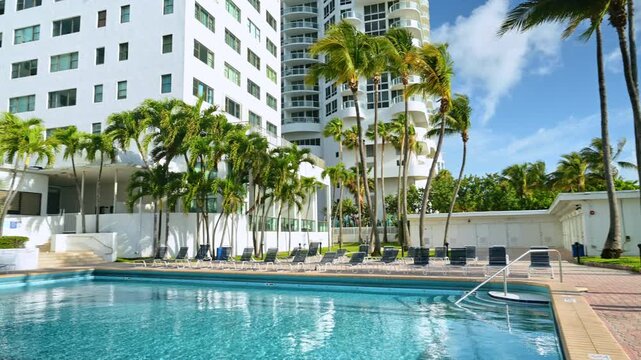 Luxury swimming pool with palm trees and hotel. Outdoor pool area of a white modern resort with sun loungers, tropical palm trees, and clear blue water.