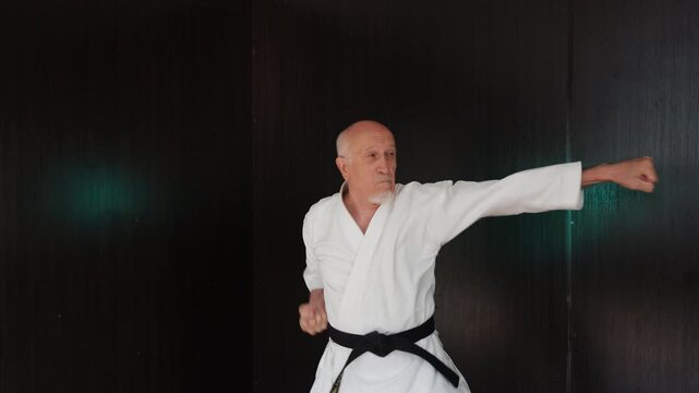 An elderly male athlete performs formal exercises against a background of flashing lights