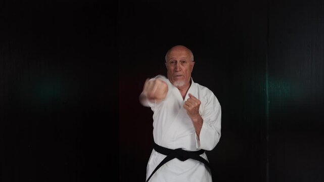 Against a background of flashing lights, an old male athlete performs punches and kicks in turn