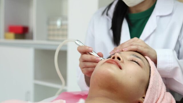The young woman relaxes during her facial treatment. The expert's hands gently cleanse her eyes, and a soft pink towel caresses her tranquil face. Her relaxed posture conveys comfort and attentive car