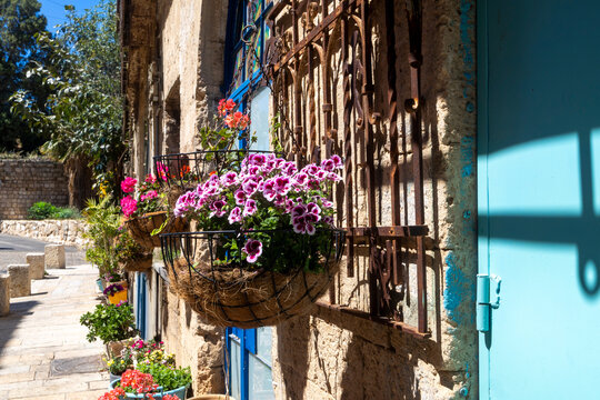Hanging flower baskets with pink geraniums on an old stone wall with a blue door