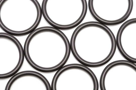 Top view macro shot of multiple black rubber O-ring seals arranged in a geometric pattern on a clean white background, showcasing industrial sealing components