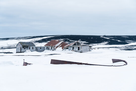 View of abandoned whaling station buildings with rusted roofs and weathered wood at Deception Island surrounded by snow and volcanic hills Antarctica.