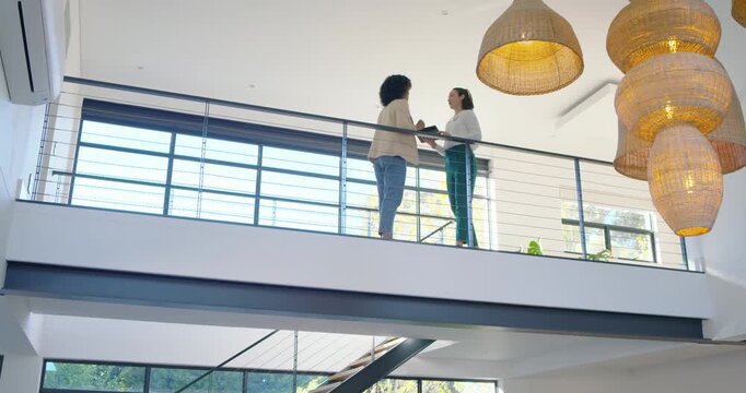 Diverse female colleagues on mezzanine touring home, holding tablet, pointing, descending staircase