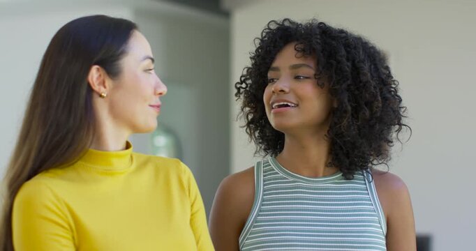 Diverse female pair in loft, smile sparking left talking in yellow top, right nodding, striped top
