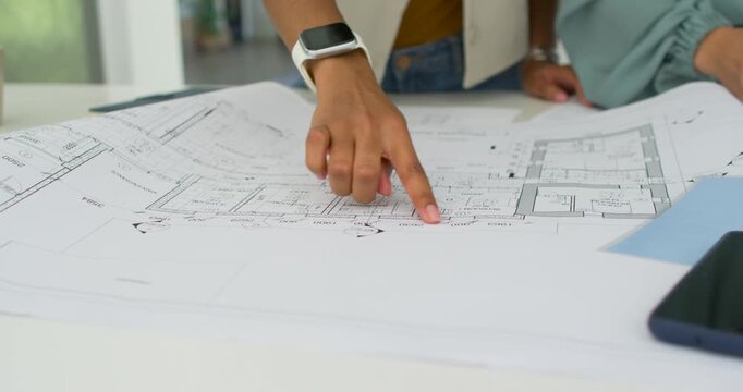 Diverse female coworkers watching while architect placing finger, tracing plans, reviewing layout