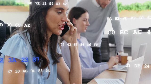 Woman receiving call, alternating typing and speaking at shared desk, code overlay aiding tech work