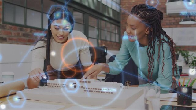 Two women leaning over design model pointing causing overlay, adjusting model for review, nodding