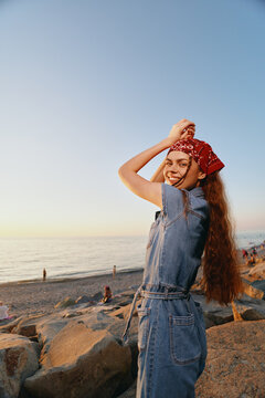 lifestyle woman in modern boho-western denim street style with red bandana smiling by the beach at sunset in warm film color tones