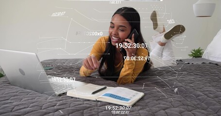 Lying woman propping elbows, talking on phone and pointing at laptop on bed, wearing mustard top © vectorfusionart