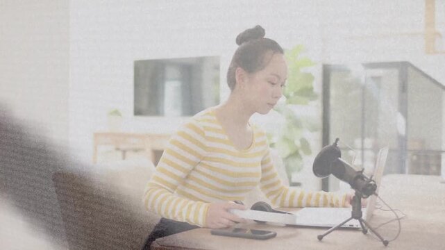 Woman picking up headphones and prepping microphone, adjusting tablet while preparing podcast