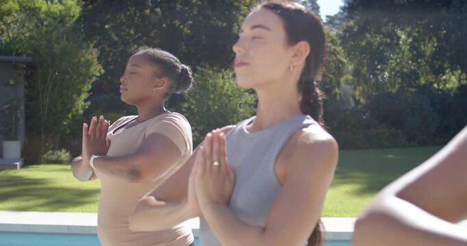3 female yogis on cue holding prayer hands, breathing by pool for calm, widening, center smiling