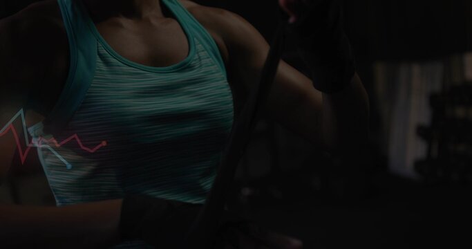 Adjusting woman tightening black hand wrap in dim gym, wearing teal striped tank top, waveform