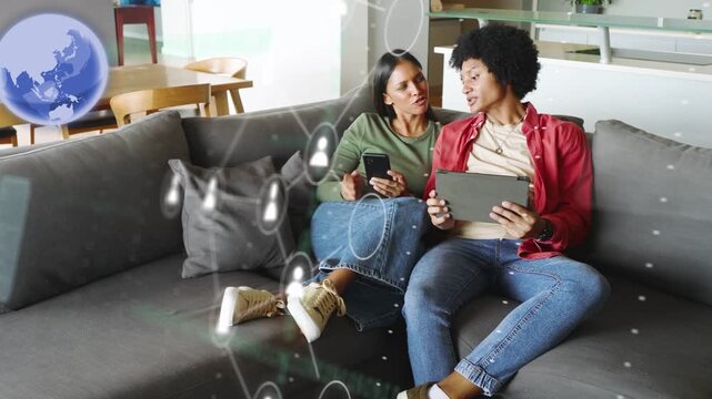 Couple sharing tablet and phone couch, tapping screens causing rotating globe nodes exploring tech