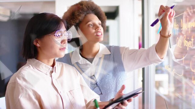 Right woman raising purple marker, writing glass for business while triangle overlays play-icon