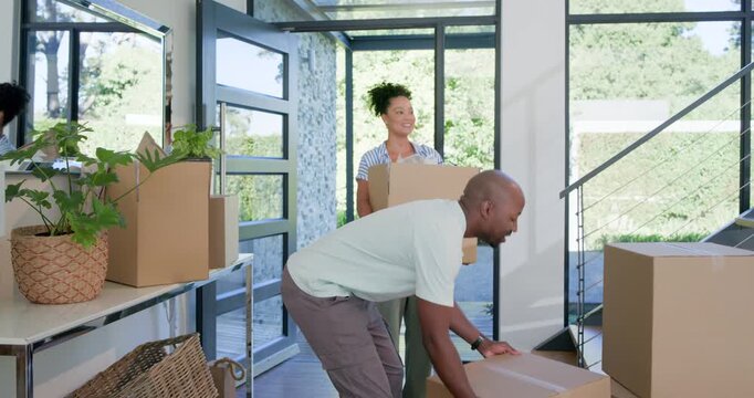 African American couple entering foyer, carrying boxes, stacking, hugging and planning move in