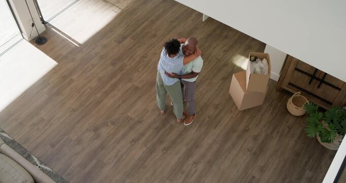 Diverse couple embracing as woman reaching, man lifting and swaying at home near move-in boxes